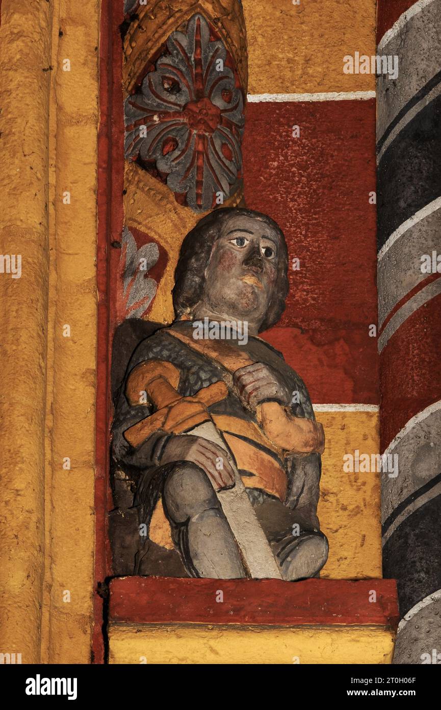 Sitzende Figur mit einem Schwert, die auf dem Hauptportal der mittelalterlichen Kathedrale St. Georg in Limburg-an-der-Lahn, Hessen, dargestellt ist. Die Figur ist wahrscheinlich St. Georg und würde, wenn ja, eine sitzende Figur des Heiligen Nikolaus ergänzen, ebenfalls auf dem Hauptportal. Diese spätromanische/frühgotische Kathedrale, die in den späten 1100er/frühen 1200er Jahren n. Chr. erbaut wurde, war zunächst zwei Heiligen geweiht, Georg und Nikolaus. Stockfoto