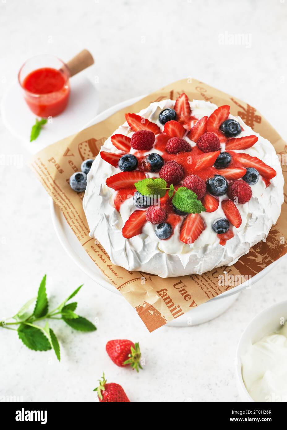 Blick von oben auf hausgemachte köstliche Meringue-Kuchen Pavlova mit Schlagsahne, frischen Erdbeeren, Heidelbeeren, Himbeeren und Erdbeersauce. Stockfoto