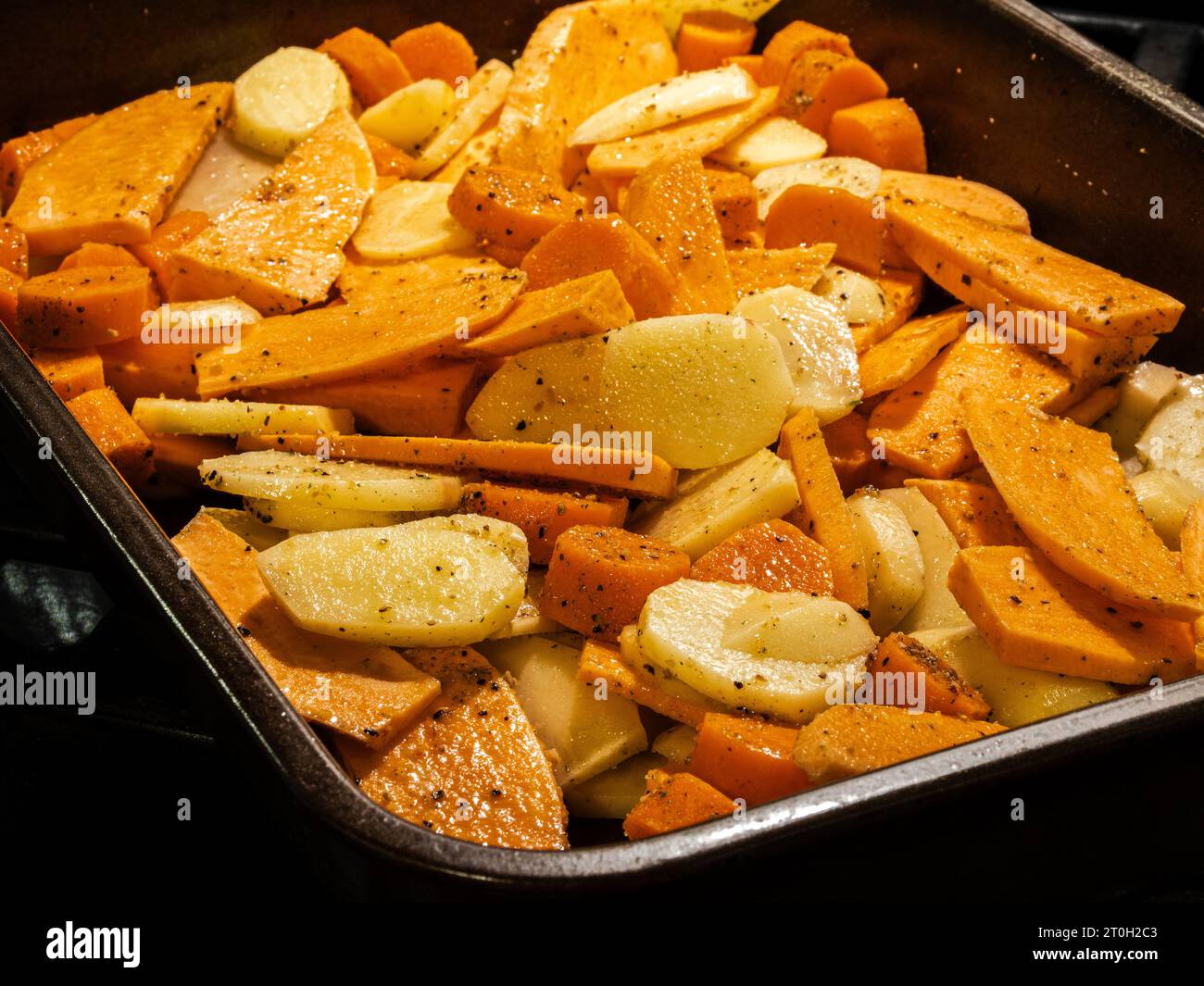 Eine nahrhafte Mahlzeit mit Süßkartoffeln, normalen Kartoffeln und Karotten, gewürzt mit Pfeffer, serviert in einer schwarzen Pfanne. Stockfoto