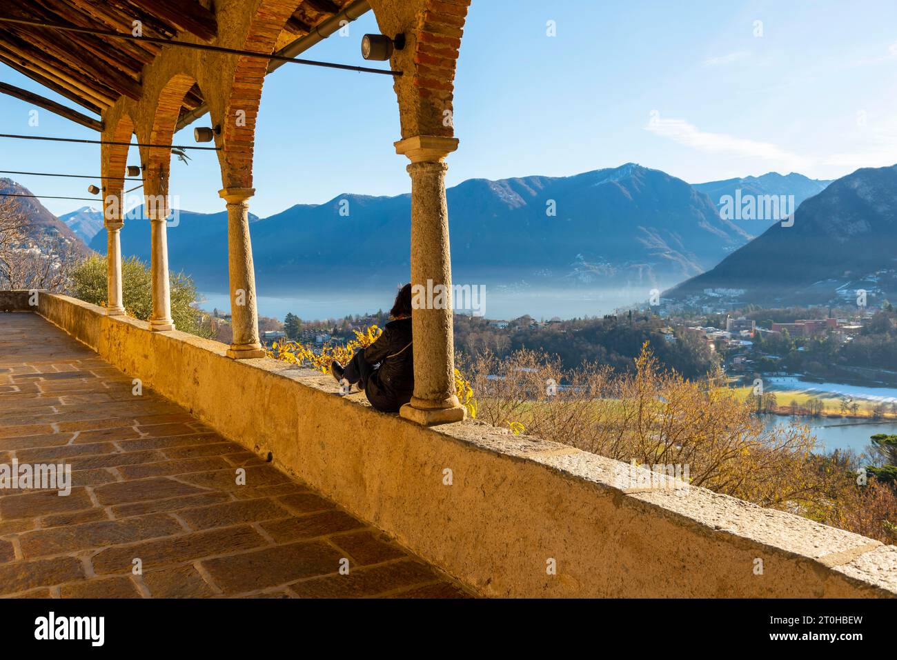 Frau Genießen Sie den Blick auf die Berge an einem sonnigen Wintertag von der Kirche dei Santi Quirico e Giulitta in Lugano, Tessin, Schweiz Stockfoto
