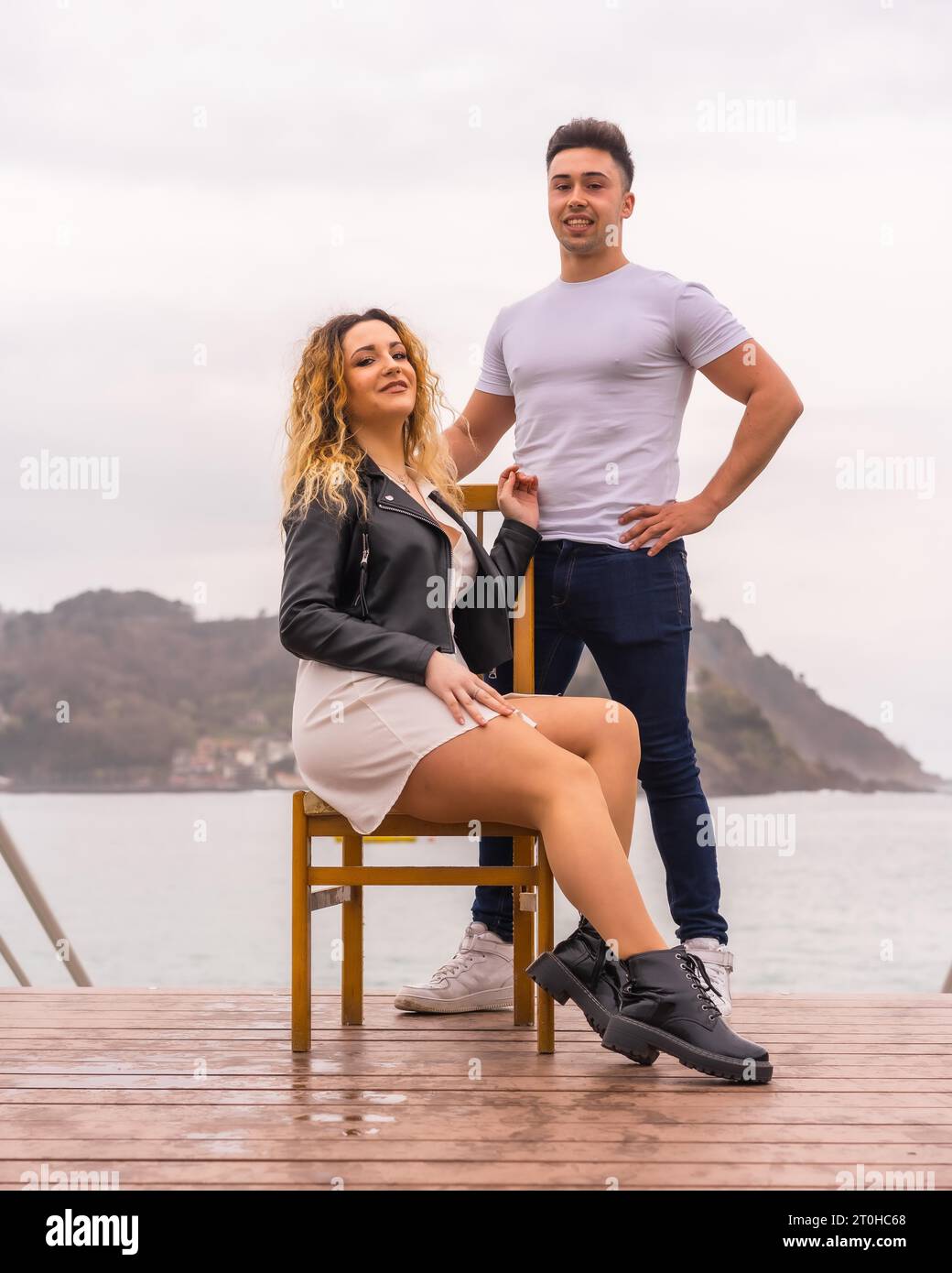 Modische Pose eines kaukasischen Paares im Urlaub am Meer. Junge Frau sitzt und Junge neben ihr Stockfoto