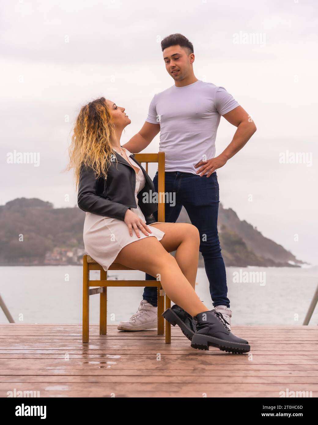 Modische Pose eines kaukasischen Paares im Urlaub am Meer. Junge Frau sitzt und Junge neben ihr Stockfoto