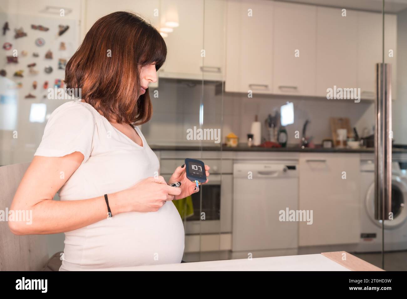 Junge Schwangere mit dem Schwangerschaftsdiabetes-Selbsttest zur Zuckerkontrolle Stockfoto