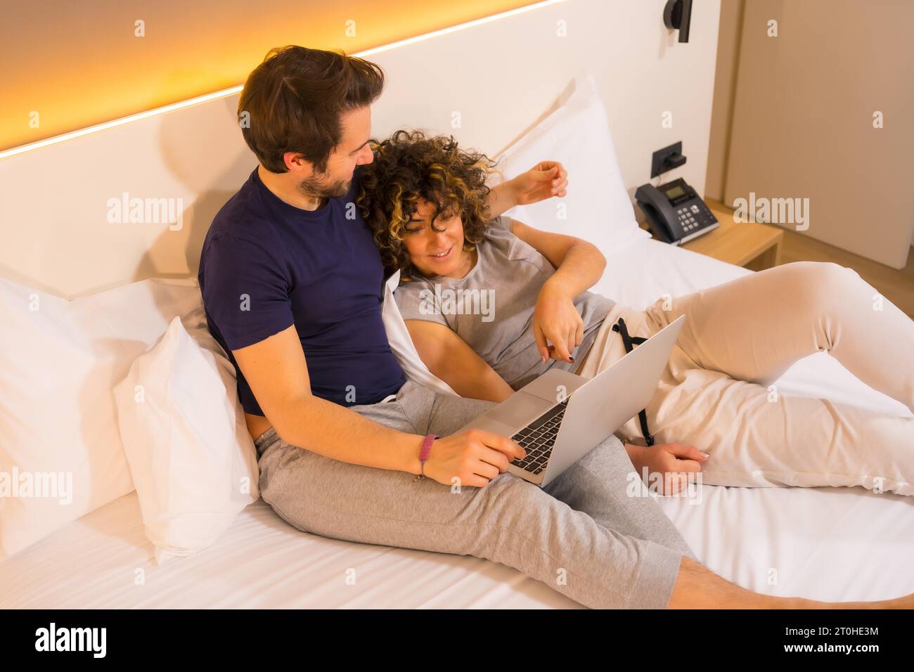 Lifestyle, ein junges kaukasisches Paar, mit Komplizen im Pyjama oben, in Pyjamas auf dem Bett, mit Blick auf den Computer Stockfoto