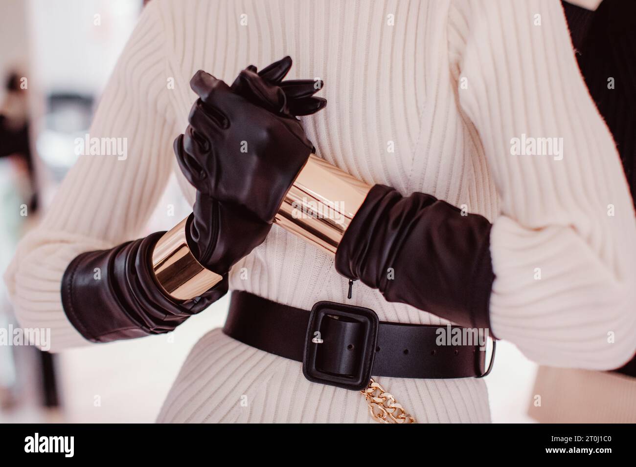 Modische Details eines gestrickten, warmweißen Pullovers, schwarzer Lederhandschuhe, Gürtel und goldene Armbänder. Damenmode und stylische Accessoires Stockfoto