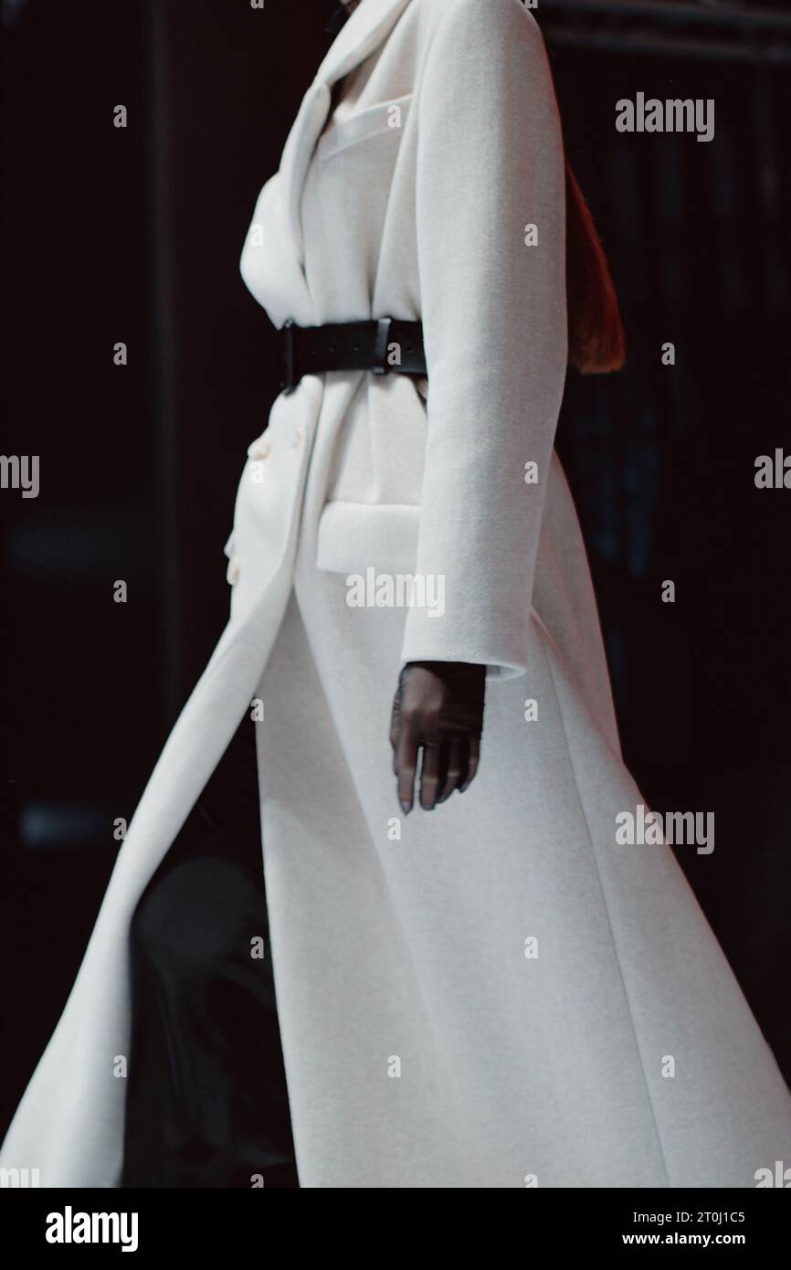 Modische Details eines langen, isolierten Wintermantels mit schwarzem Gürtel. Modemodell, das auf schwarzem Hintergrund läuft Stockfoto