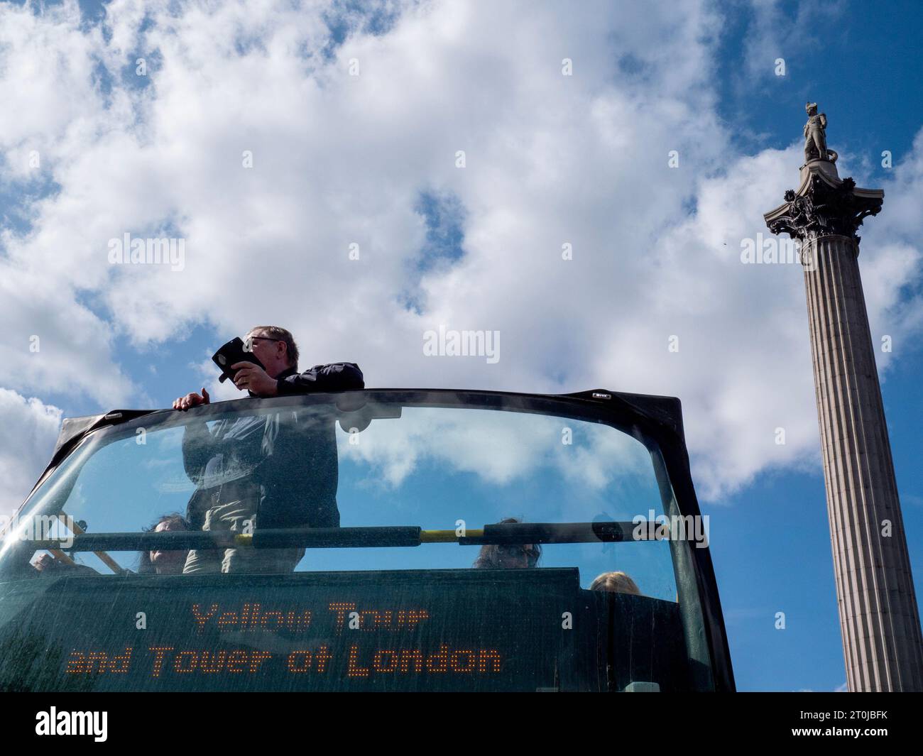 Ein Tourist auf dem offenen Oberdeck eines Tootbus-Sightseeing-Busses macht Fotos auf seinem Handy, während er an der Nelson's Column am Trafalgar Square, London, vorbeifährt Stockfoto