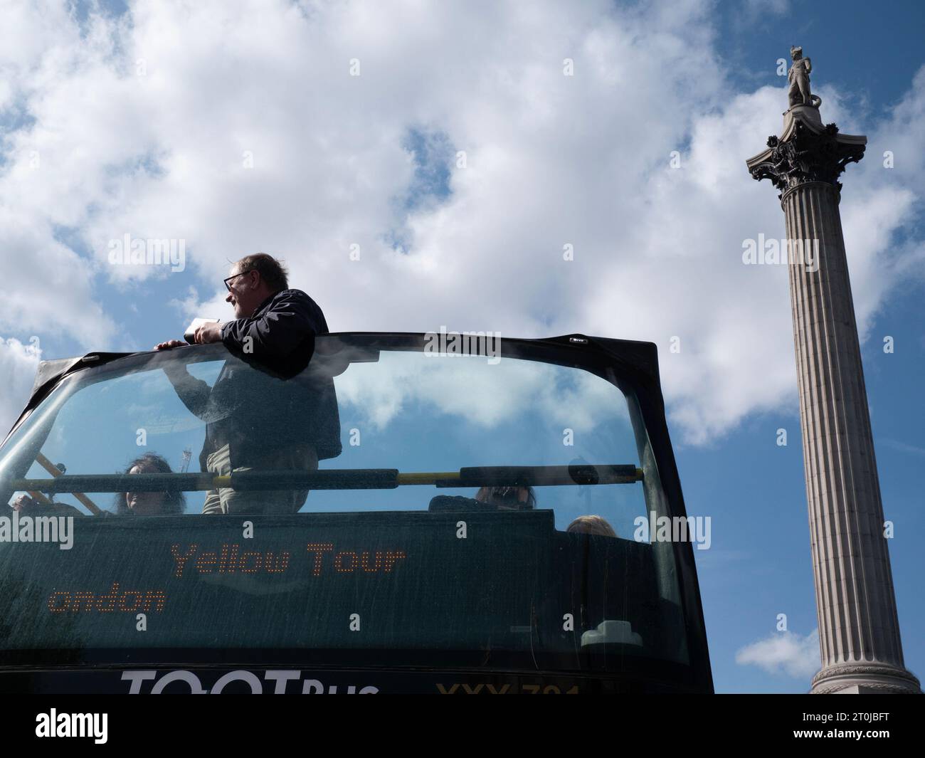 Ein gelber Sightseeing-Bus mit offenem Oberdeck, der von Tootbus betrieben wird, bringt Touristen unter klarem blauen Himmel an der Nelson's Column am Trafalgar Square vorbei Stockfoto