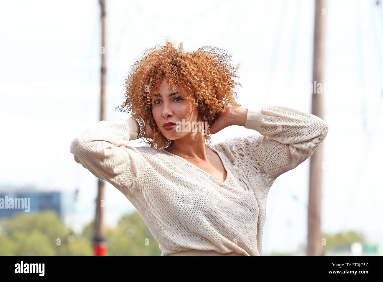 Porträt einer Frau im weißen Pullover, die ihr lockiges Haar hält Stockfoto