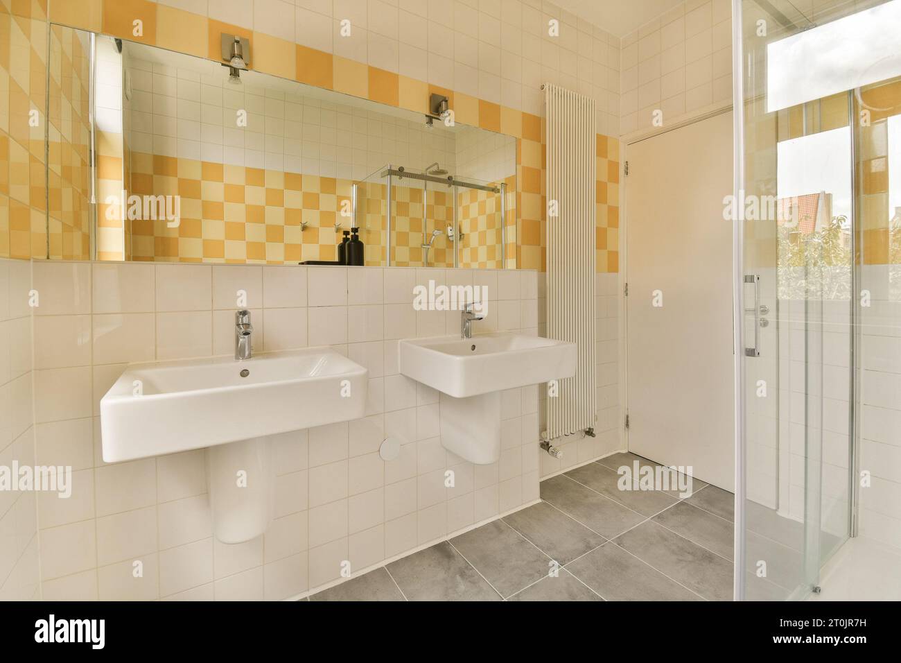 Ein Badezimmer mit gelben und weißen Fliesen an den Wänden, zwei Waschbecken und eine Duschkabine davor Stockfoto