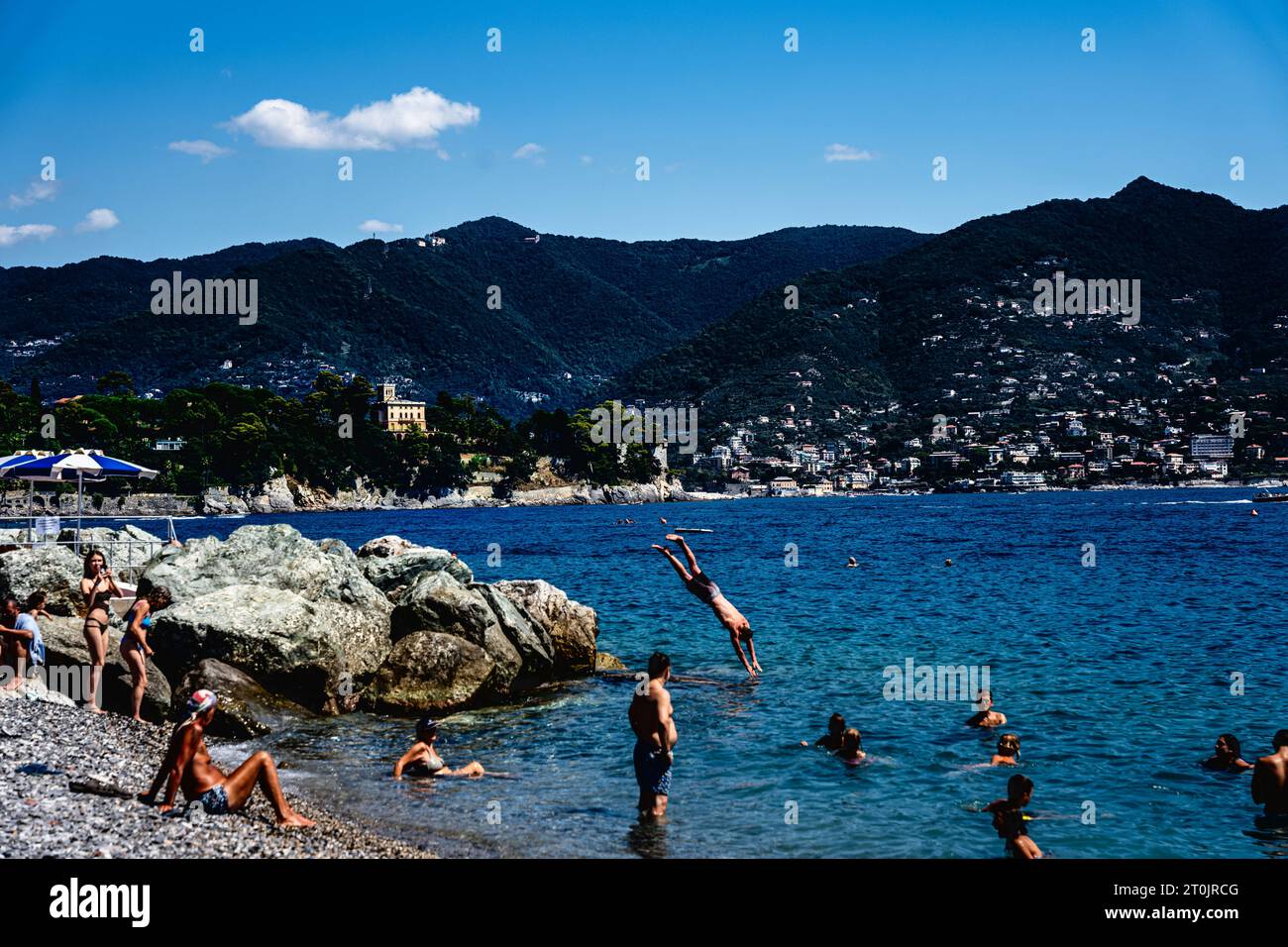 Genießen Sie Santa Margherita Italien beim Schwimmen und Tauchen in das Meer von Ligurien an einem heißen, sonnigen Sommertag mit Felsen und üppigen Bergen unter der Sommersonne Stockfoto