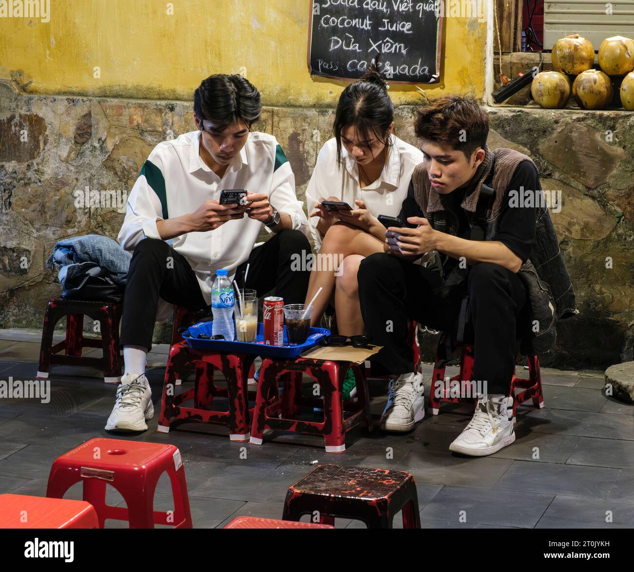 Hoi An, Vietnam. Drei junge Leute, die in ihre Handys vertieft waren, während sie Erfrischungen tranken. Stockfoto