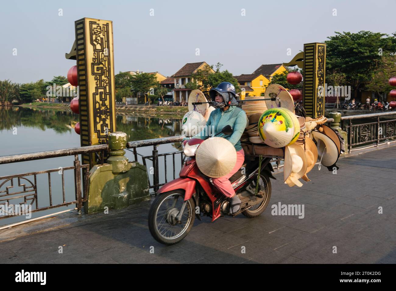 Hoi An, Vietnam. Verkäufer auf der Fußgängerbrücke über den Fluss Thu Bon, am frühen Morgen. Mit Kollektion von Hüten zum Verkauf. Stockfoto