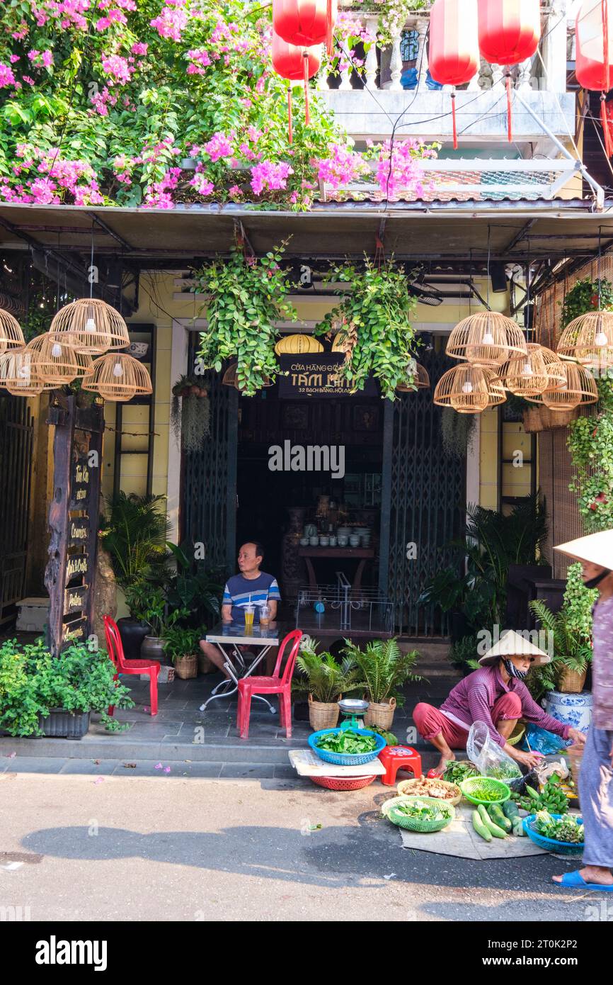 Hoi An, Vietnam. Café-Patronin wartet auf Frühstück, während Street Gemüsehändler ihre Produkte zum Verkauf bereithält. Stockfoto