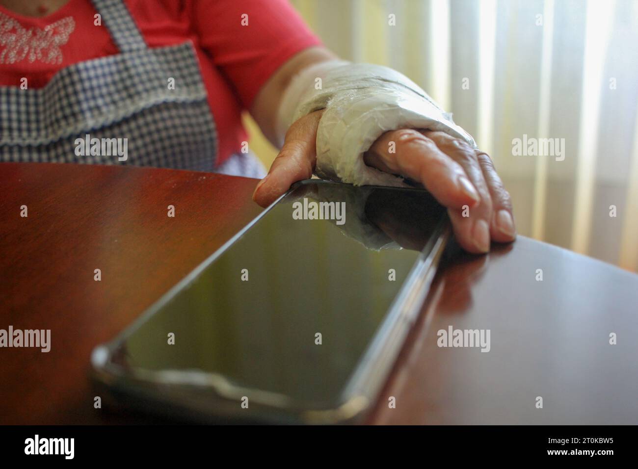 Frau mit eingegossenem Handgelenk, die zu Hause ein Handy schnappt Stockfoto