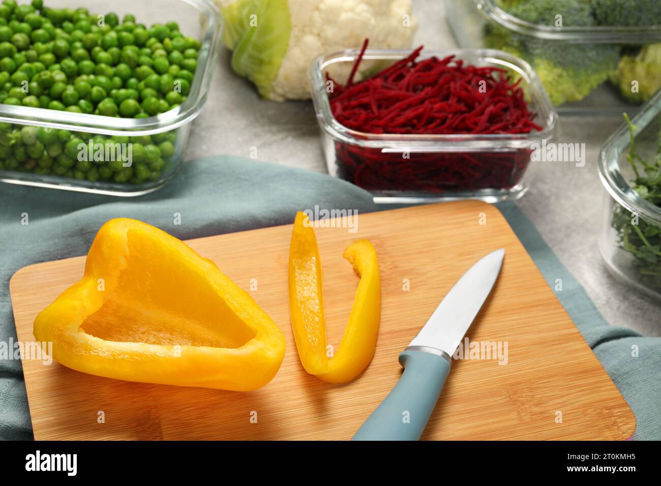 Schneiden Sie Paprika, Messer und Behälter mit frischen Produkten auf einem hellgrauen Tisch. Lagerung von Lebensmitteln Stockfoto