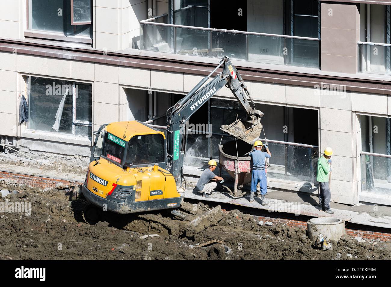 An einem sonnigen Tag entlädt eine Gruppe von Bauarbeitern vorgemischten Zement, der von einem Gabelstapler in der Nähe des im Bau befindlichen Gebäudes gebracht wird. Stockfoto