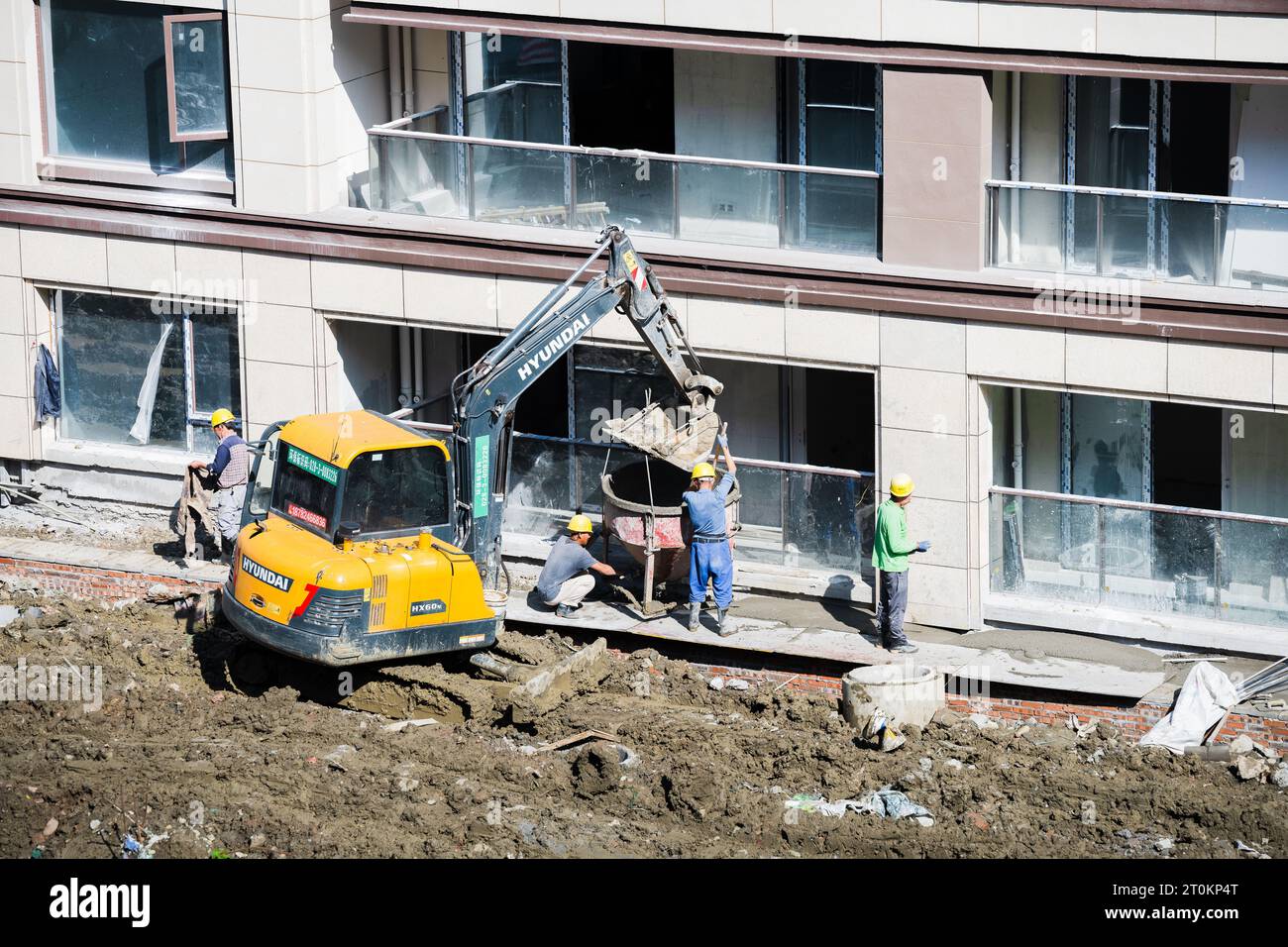 An einem sonnigen Tag entlädt eine Gruppe von Bauarbeitern vorgemischten Zement, der von einem Gabelstapler in der Nähe des im Bau befindlichen Gebäudes gebracht wird. Stockfoto