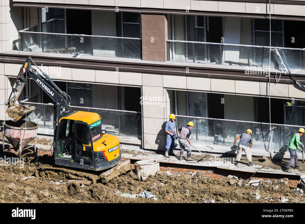 An einem sonnigen Tag entlädt eine Gruppe von Bauarbeitern vorgemischten Zement, der von einem Gabelstapler in der Nähe des im Bau befindlichen Gebäudes gebracht wird. Stockfoto