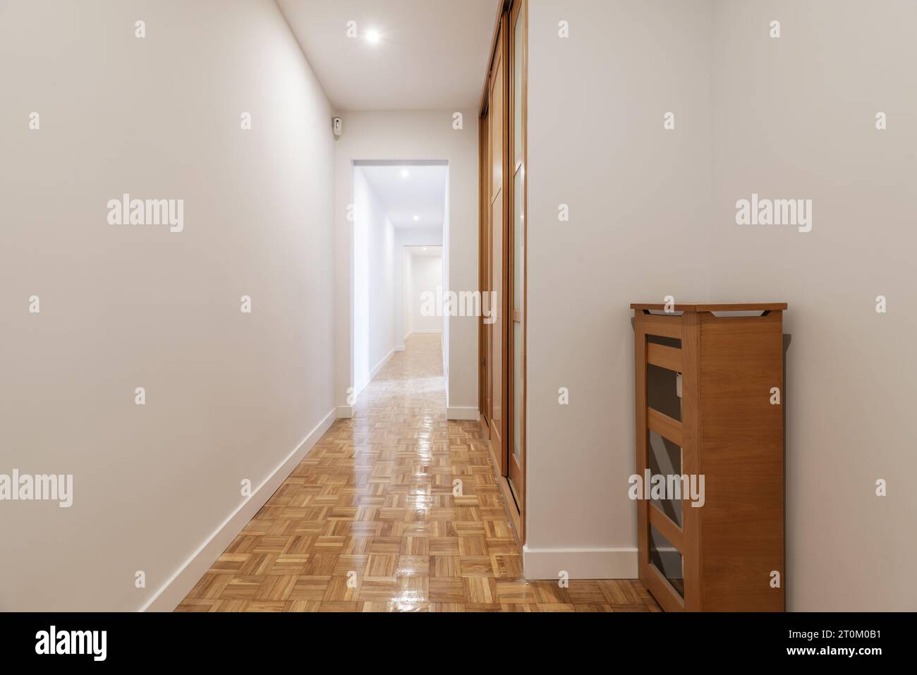 Eingangshalle eines Hauses mit Heizkörperabdeckung, eingebautem Kleiderschrank, langem Flur mit frisch gestrichenen glatten weißen Wänden und Parkettboden Stockfoto