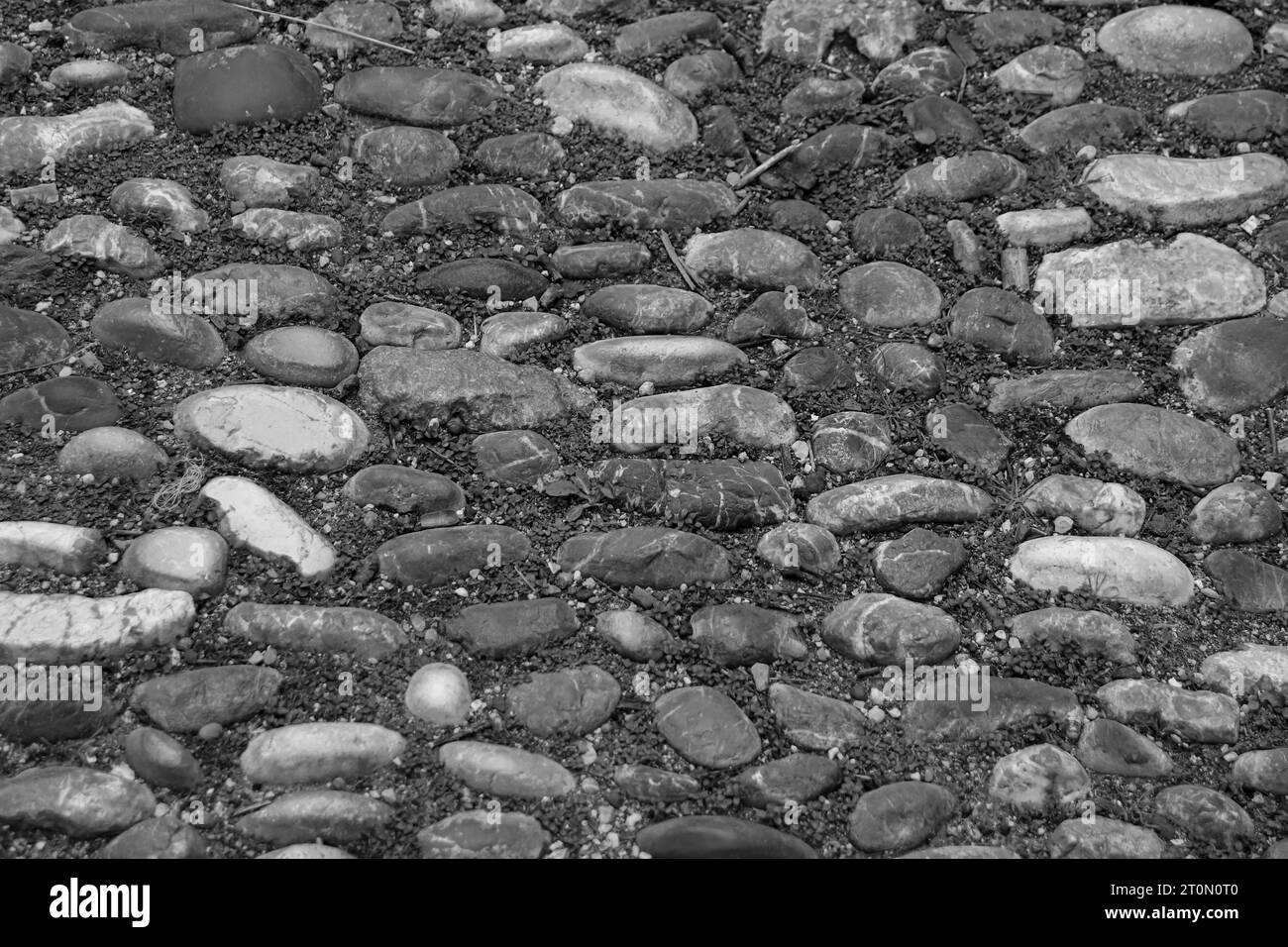 Schwarz-weißer abstrakter Hintergrund des runden Kopfsteinpflasterfelsens Wanderweges mit Gras dazwischen in Rhodos, Griechenland Stockfoto