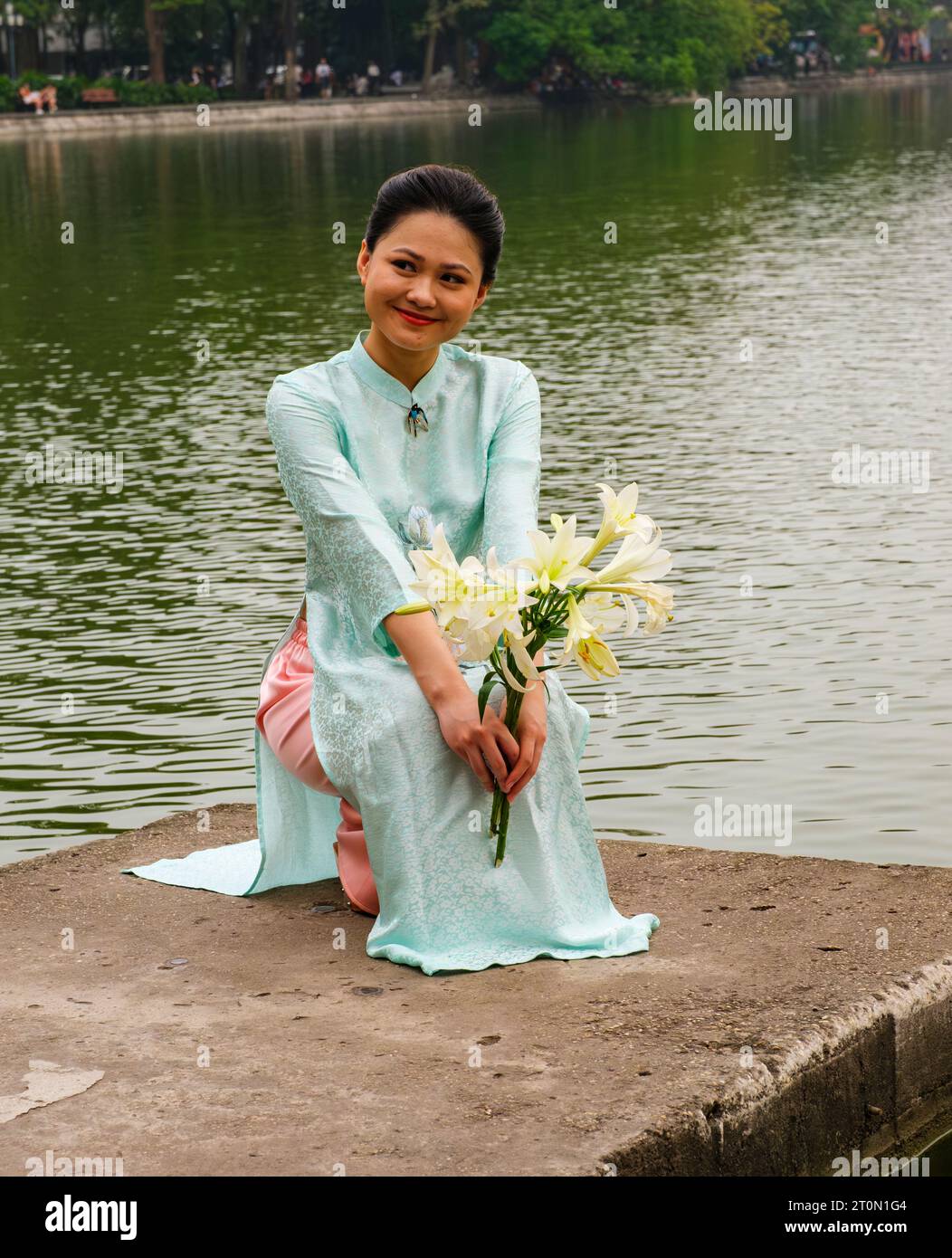 Hanoi, Vietnam. Eine junge Frau, die einen Ao Dai am Lake Hoan Kiem trägt. Stockfoto
