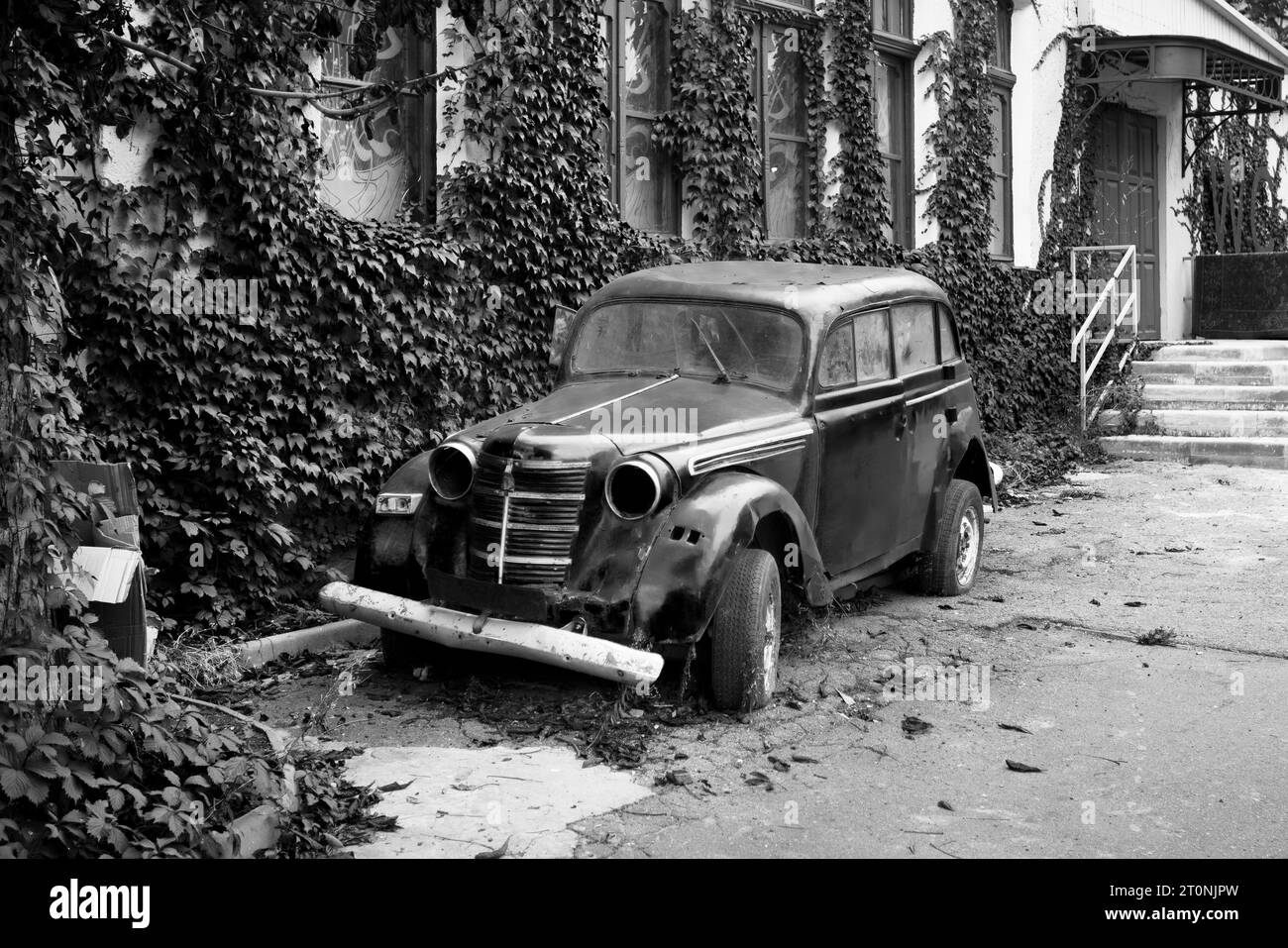 Schwarz-weiß-Foto eines Retro-Autos, der in der Nähe des Hauses steht. Altes, rostiges Auto. Stockfoto