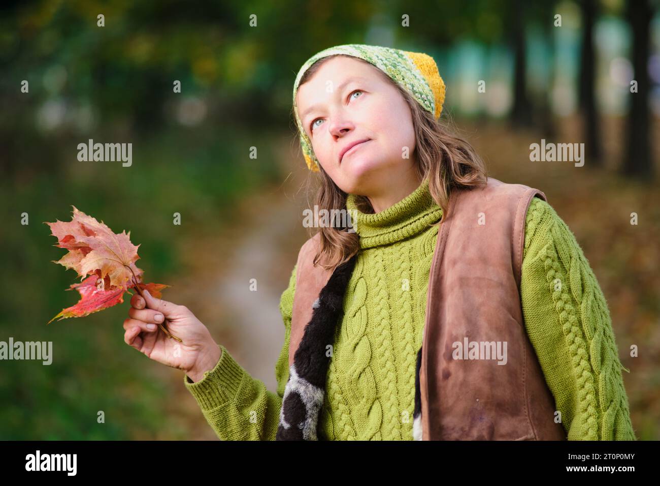 Porträt einer Frau in Strickmütze und Pullover mit Herbstlaub. Porträt einer Frau im Alter von 52 Jahren Stockfoto