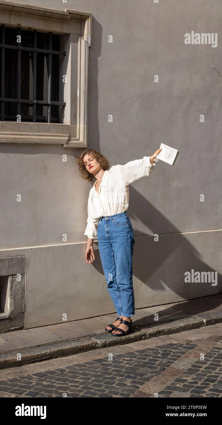 Junge Frau, die sich in der Warschauer Altstadt an eine Mauer lehnt und eine Kopie von Kameliowy Sklep Papierniczy von Ito Ogawa hält Stockfoto