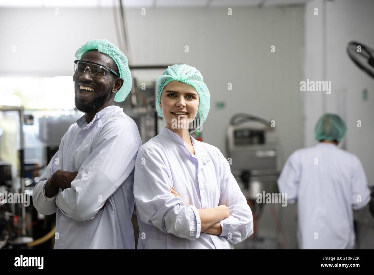 Porträt glücklicher schwarzer Arbeiter lachen lächelnd zusammen mit einer Freundin, die den Arm überkreuzt hat und in der Lebensmittel- und Getränkefabrik mit Hygiene arbeitet Stockfoto