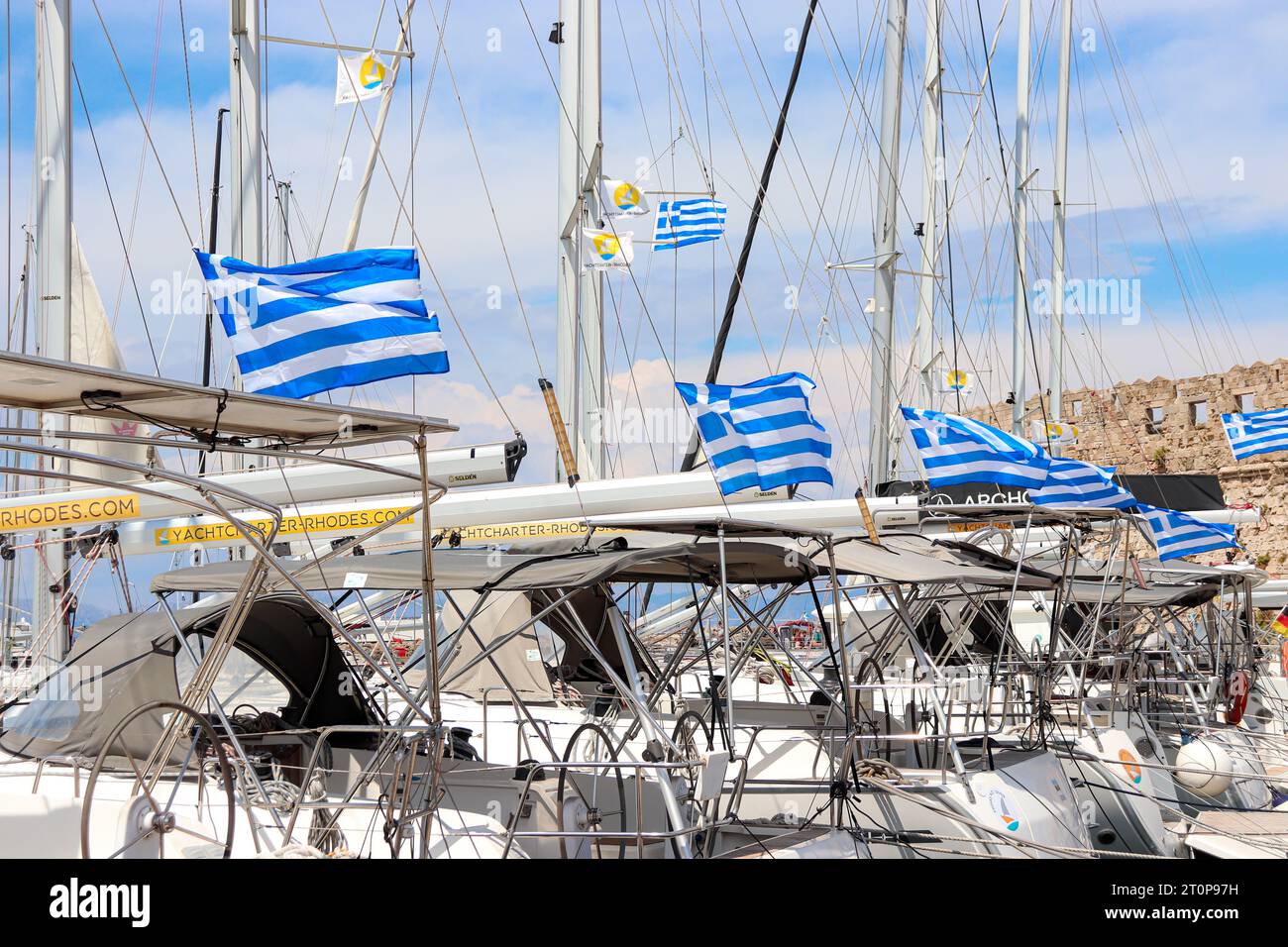 Eine Reihe offener im Wind hing die griechische Nationalflagge an den angedockten Yachtbooten entlang des Hafens von Mandraki Stockfoto