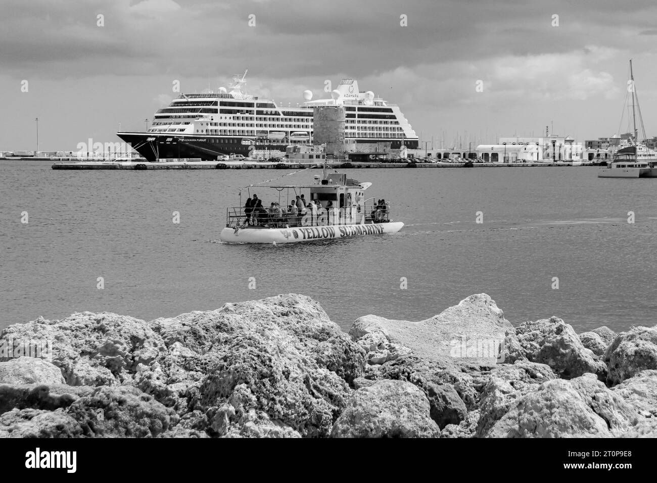 Das Kreuzfahrtschiff Azamara Pursuit legte im Hafen von Rhodos hinter einer gelben U-Boot-Tour in Schwarz-weiß an Stockfoto