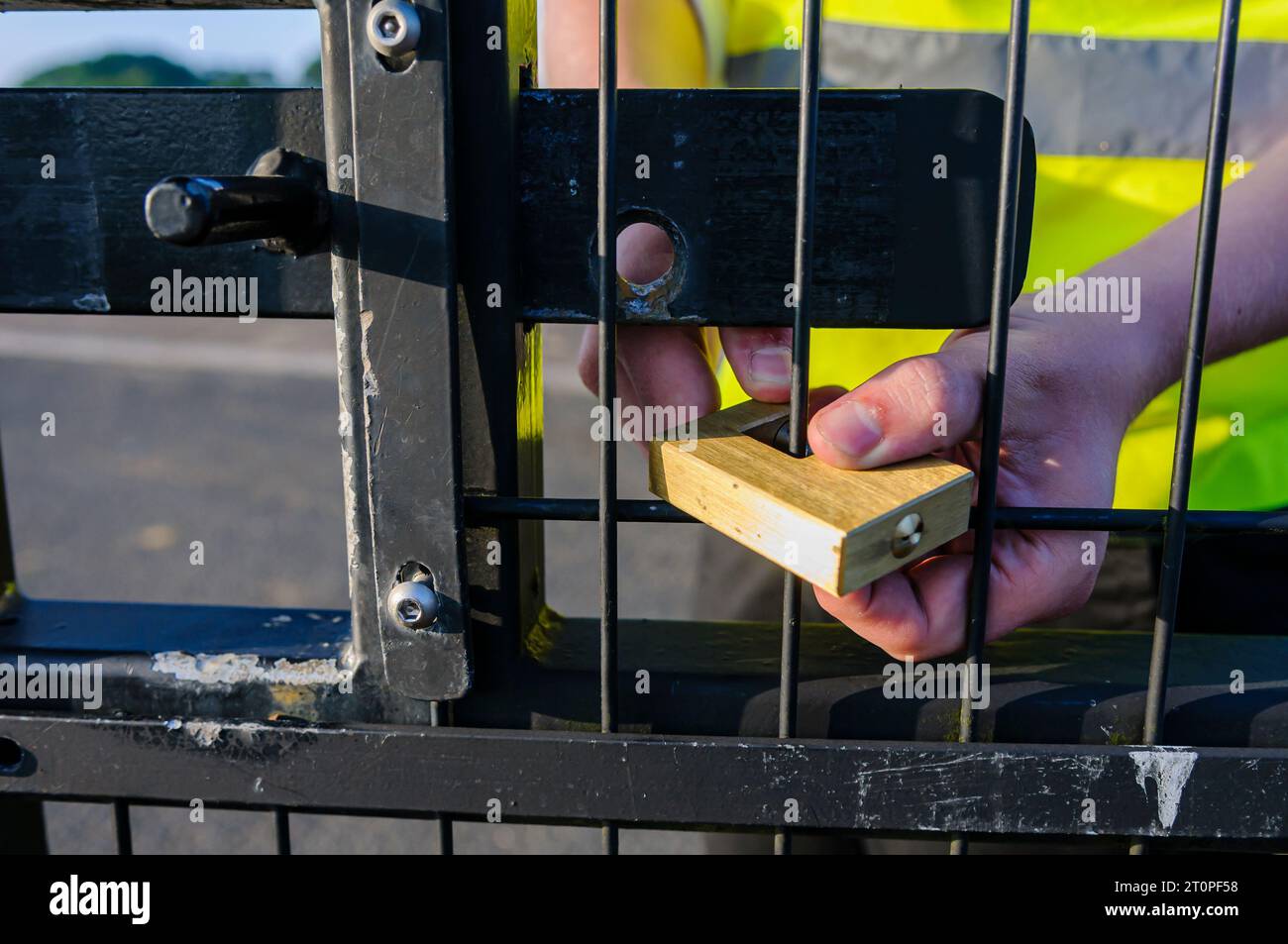 Ein Wachmann legt eine Sperre auf ein Tor nach dem Entriegeln der Schraube Stockfoto