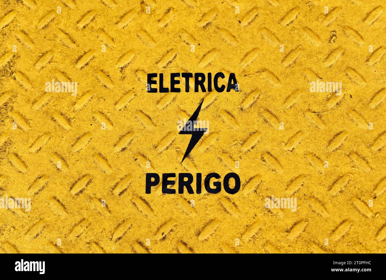 Gelbe metallische Oberfläche mit portugiesischen Wörtern, die ELETRICITY und DANGER bedeuten (Eletrica Perigo) Stockfoto