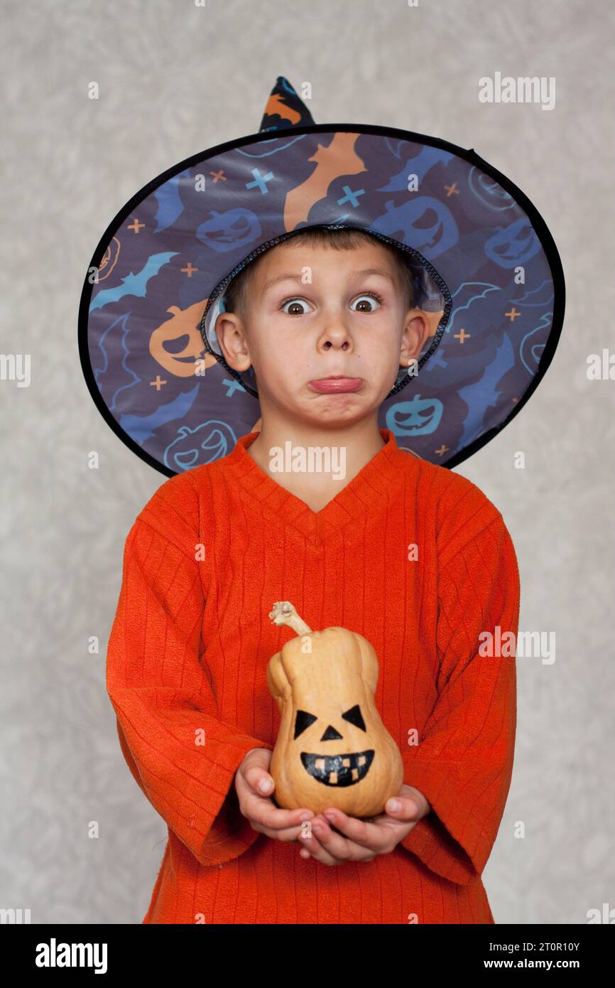 Frohes Halloween. Porträt eines niedlichen Vorschuljungen mit Hexenhut, der kleine Jack-o-Laterne hält und grimmig ist. Festliche lustige Party zu Hause. Stockfoto