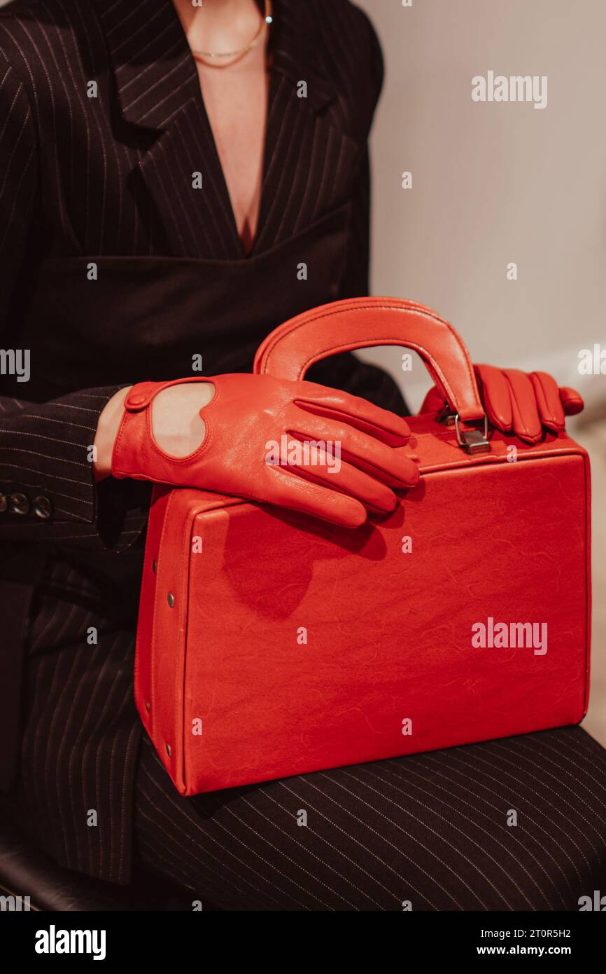 Weibliche Hände in Lederhandschuhen, die eine klassische, hellrote Handtasche halten. Modische Aufnahme. Vertikal Stockfoto