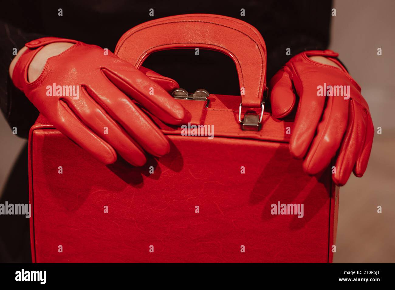 Weibliche Hände in Lederhandschuhen, die eine klassische, hellrote Handtasche halten. Modische Aufnahme Stockfoto