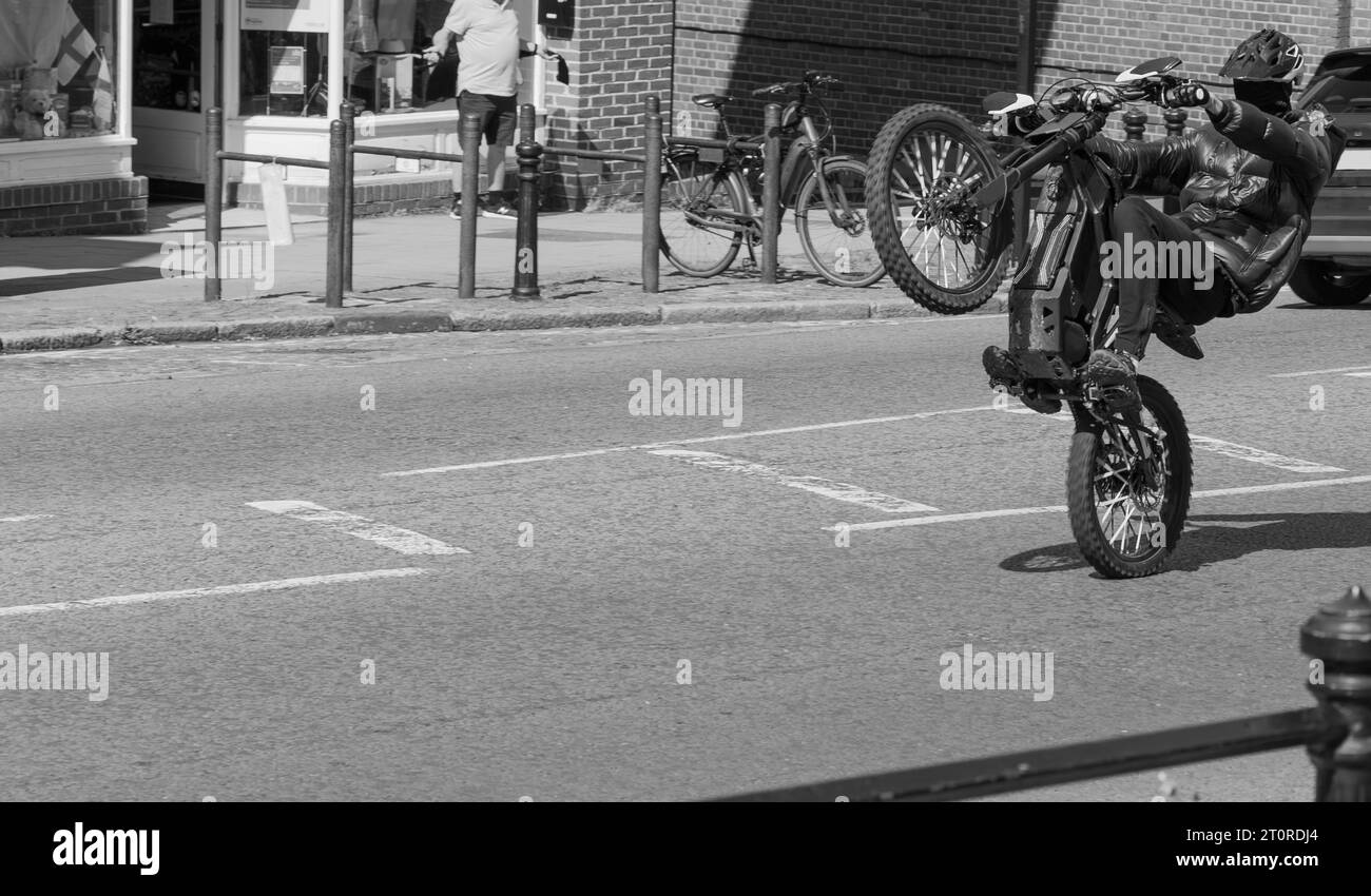 Ein unbekannter Fahrer führt ein Elektro-Bike-Wheelie auf der lokalen High Street auf. Stockfoto