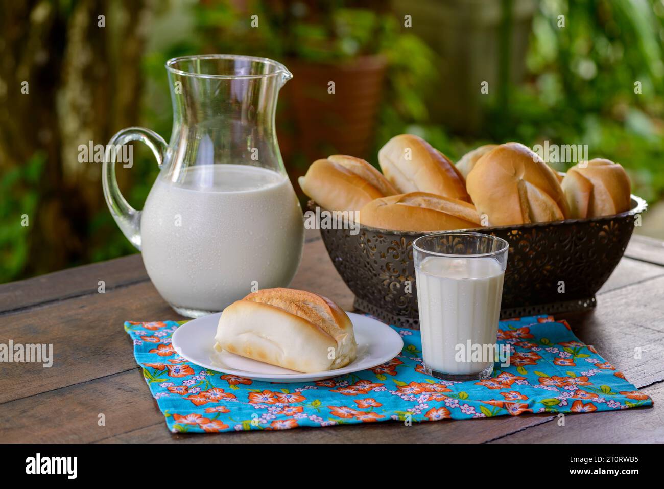 Brot in einem Korb und Milch in einem Glaskrug auf einem Holztisch. Stockfoto