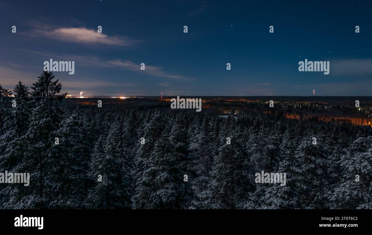 Verschneite Wälder mit weit entfernten Stadtlichtern im Winter in Finnland Stockfoto