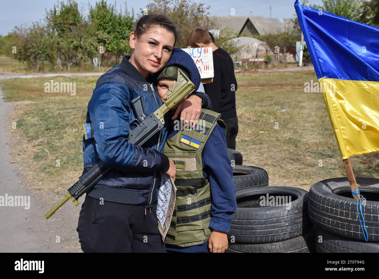 Bilenke, Ukraine. Oktober 2023. Mutter umarmt ihren Sohn, während er die Spielzeugmaschinenpistole des Sohnes hält, während ein Junge vorgibt, ein Territorialverteidiger zu sein, am Spielkontrollpunkt im Dorf Bilenke in der Region Zaporischschschhia. Alle ukrainischen Kinder sind tief vom Krieg betroffen. Viele haben ihr Leben radikal verändert, weil sie ihre Häuser verloren haben oder gezwungen wurden, zu evakuieren. (Foto: Andriy Andriyenko/SOPA Images/SIPA USA) Credit: SIPA USA/Alamy Live News Stockfoto