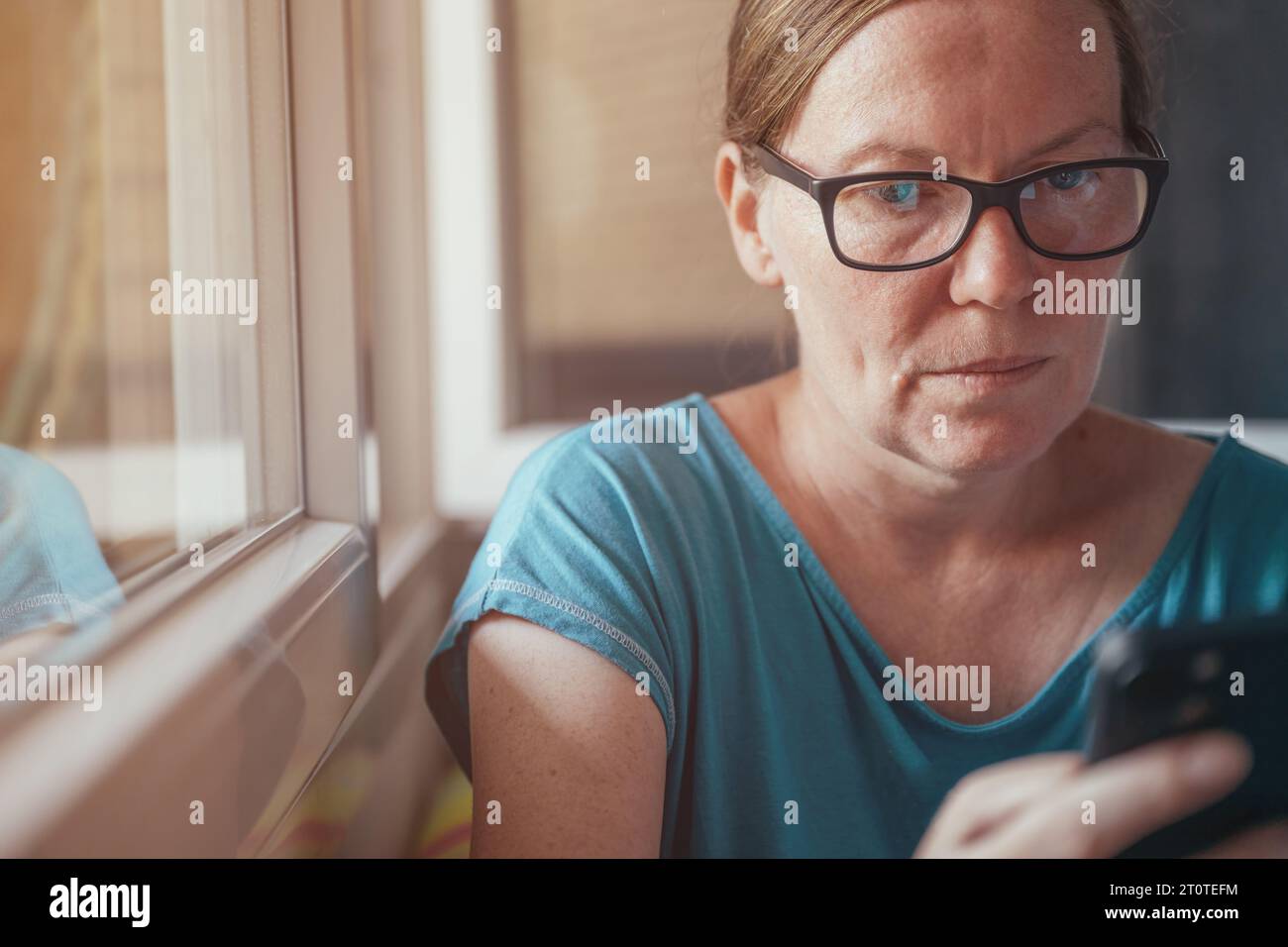Ernste Erwachsene Frau, die aus ihrem Schlafzimmer auf dem Handy schreibt, selektiver Fokus Stockfoto