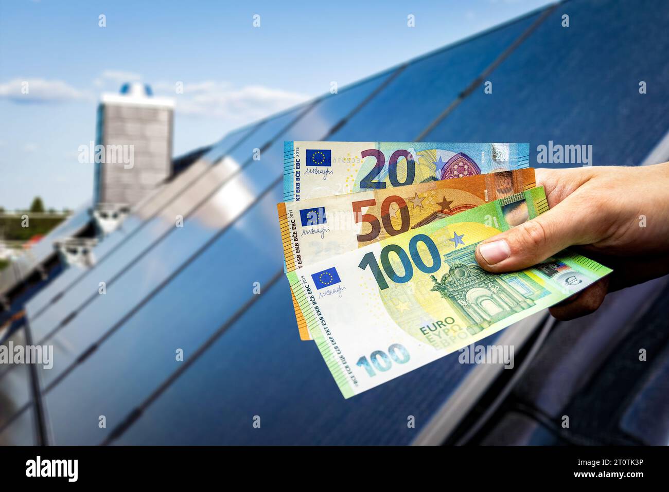 Euro-Banknoten in der Hand, mit Solarpaneelen auf einem Haus im Hintergrund Stockfoto