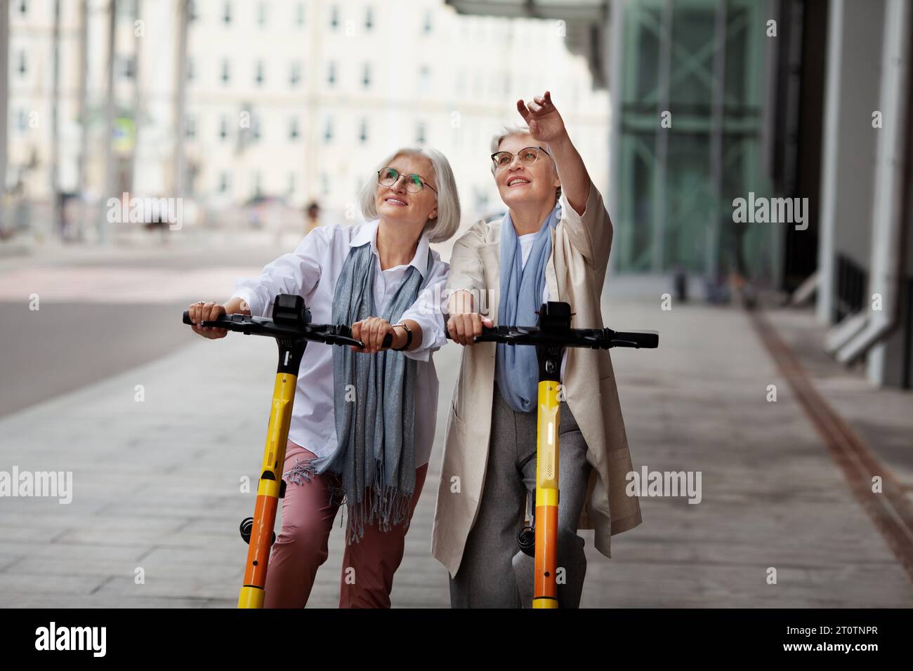 Porträt zufriedene ältere Frauen mit grauem Haar, die gemeinsam auf elektrischen Rollern im Freien fahren. Ältere Freundinnen erkunden die Stadt auf einem Ausflug, Stockfoto