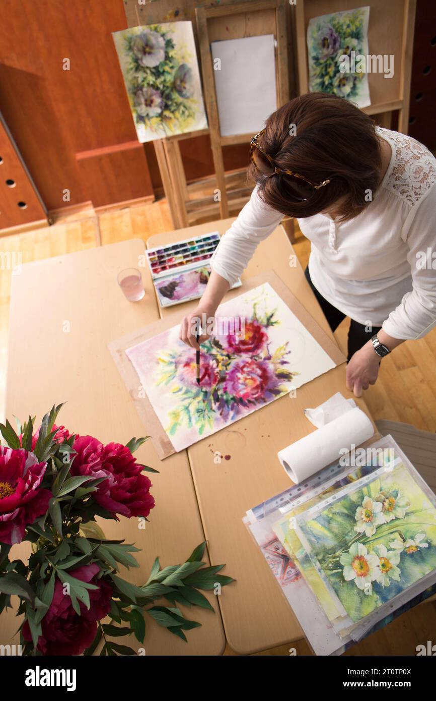Die Künstlerin malt einen Frühlingsstrauß aus Pfingstrosen in ihrem Atelier, von oben Stockfoto