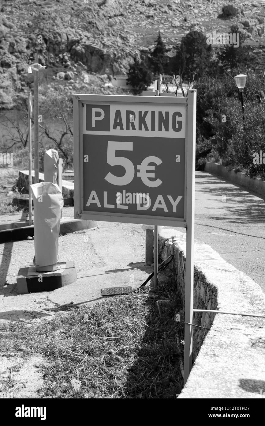 Ein Parkschild informiert die Fahrer über eine Gebühr von 5 € für das ganztägige Parken am St. Paul's Bay Beach auf Rhodos Island, Griechenland in Schwarz-weiß Stockfoto