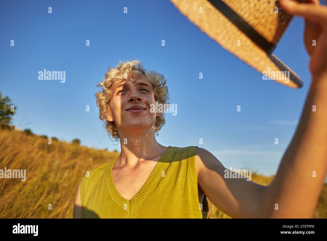 Ein lächelnder junger Mann bedeckte sein Gesicht vor der Sonne mit einem Strohhut Stockfoto