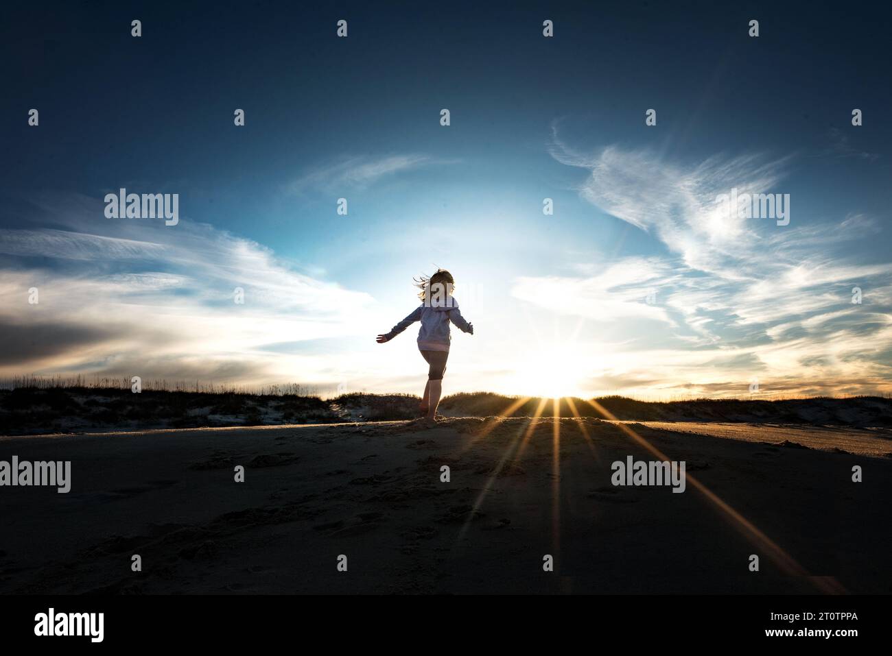 Ein junges Mädchen, das unter blauem Himmel in Richtung Sonnenuntergang läuft Stockfoto