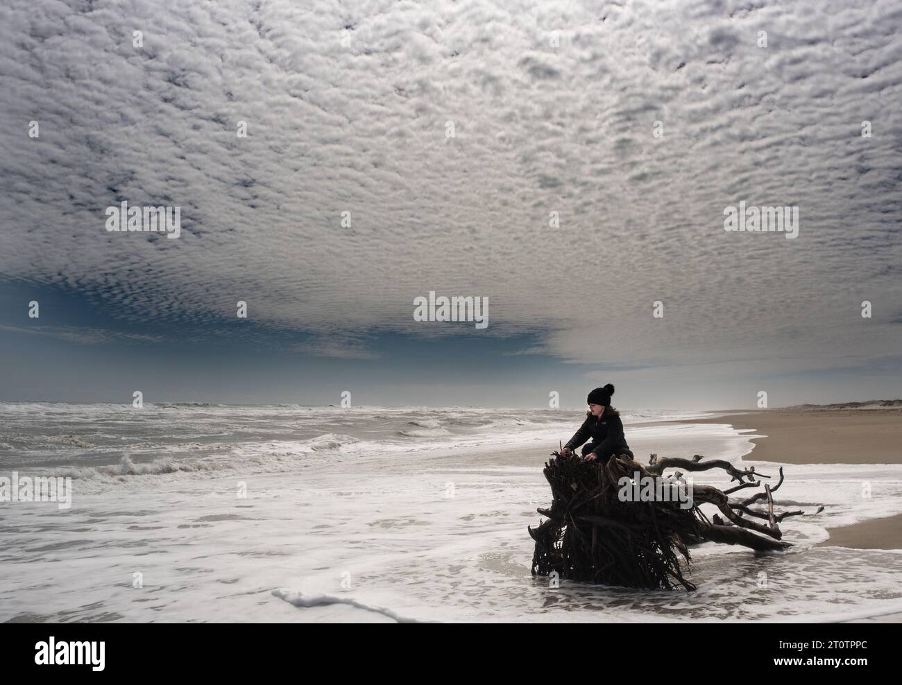 Ein junges Mädchen, das bei Flut in rauen Meereswellen sitzt Stockfoto