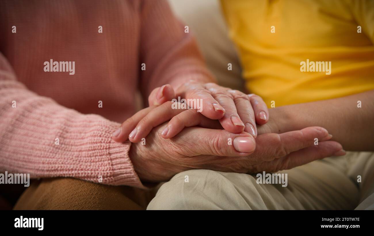 Nahaufnahme weiblicher älterer Hände, die Hand des Kindes halten unerkennbar liebevolle, zärtliche Großmutter unterstützen Enkel, der zusammen auf der Couch sitzt Stockfoto